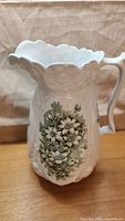 Front view of ceramic pitcher showing embossed floral design and green floral pattern
