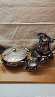 Silver-plated pot with lid, creamer dish in front, and pitcher on decorative tray base.