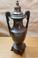 Front view of brass trophy style urn showing lid, body, handles, and base.