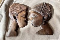 Front view of two wood carved head profiles facing each other, male and female, showing facial and hair detail.