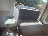 Tall gray upholstered bench with tufted back and seat next to a gray swivel bar stool by a window.