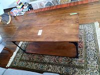 Coffee table top and lower shelf showing wood grain and metal frame from side angle, with rug and furniture in background.
