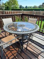 Outdoor round metal framed table with glass top and lattice design on a wooden deck, surrounded by patio chairs.