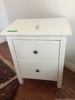 Front view of white two drawer night table showing overall condition and two black knob handles.