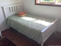 Full view of assembled white twin bed frame with green bedspread and two pillows in corner of room