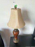 Full view of one lamp showing beige fabric bell-shaped shade and urn-shaped wooden base with ornate metal accents at top and bottom.