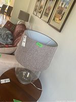 Full view of one lamp showing clear plexiglass base, grey textured fabric cylindrical shade, measuring approximately 17x25 inches.