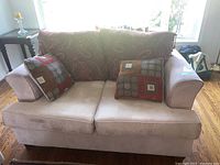 Front view of beige faux suede loveseat with two decorative square cushions and a large paisley throw.