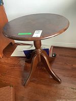 Front side view of round wooden occasional table showing tabletop and pedestal base with three legs on hardwood floor