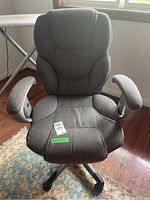 Front view of gray upholstered office chair showing cushioned backrest, seat, and padded armrests with five casters at base.