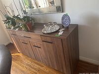 Front view of the wood grain sideboard showing one drawer and four doors with black metal handles, decorative items on top removed for sale.