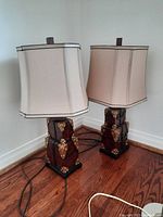 Two table lamps with beige hexagonal fabric shades and faux wood trunk bases placed on hardwood floor. Lamps powered by visible cords. Minor wear visible on shades and bases.