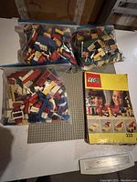 Three large resealable plastic bags filled with assorted vintage Lego bricks and pieces of various shapes and colors, a vintage Lego instruction booklet labeled 222, and a large green Lego baseplate.