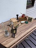 Photo of antique curiosities on wooden table including clocks, bottles, boxes, oil can, and other vintage items