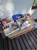 Wide view showing multiple open boxes holding assorted Christmas decorations such as ornaments, figurines, and tree toppers on a wooden surface outside.