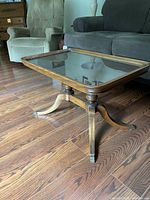 Glass top coffee table showing wood frame, glass surface, and one side with a leg ending in metal claw foot.