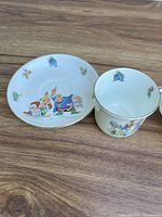 Porcelain cup next to its matching saucer on a wood surface, showing detailed colorful storybook characters from Prince David Princess Glory series by Hammersley England.