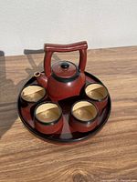 Tea set displayed including one teapot, four tea cups, and a round serving tray on a wooden surface.
