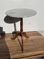 Photo of small pedestal table with round white marble top and wooden base with three curved legs in natural light against a white wall.