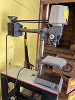 Side view of gray Rockwell radial drill press showing motor, radial arm, on/off switch, and worktable on stand.