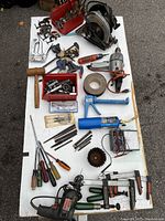 Overview of power and hand tools arranged on a white surface including clamps, screwdrivers, sockets, a skill saw, drill, and caulking gun.
