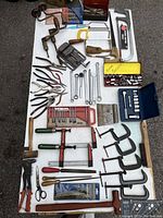 Top-down view of entire lot showing layout of tools including pliers, clamps, saws, drill bits, sockets and hand braces on white surface