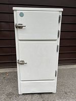 Front view of closed white enamel ice box with two doors and chrome hinges