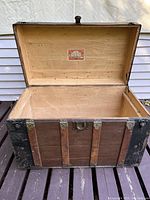 View of open antique wooden trunk showing interior and sailboat label under lid