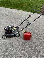 Full lawn mower with red gas can on driveway surface, showing the entire mower with handle and wheels