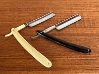 Photo of two straight razors placed on a wooden surface, showing blade and handles with one black and one ivory handle