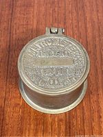 Top view of brass trinket box lid showing embossed 'METROMETER CO TRIDENT WATER METER NEW YORK'