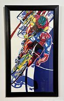 Full view of framed colorful cycling art print showing three cyclists in vibrant colors and black frame.