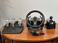 Full view of the Logitech G27 racing wheel, pedals, and shifter laid out on a table showing all parts in good condition.