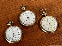 Three pocket watches laid out showing front dials