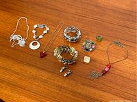 Overview of various costume jewelry including bracelets, rings, pendants, and necklaces arranged on a wooden surface.
