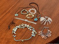 Overview of various costume jewelry pieces displayed on wooden surface, including necklaces, bracelets, and one watch with turquoise, metallic, clear and colorful bead details.