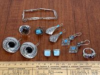 Full lot of sterling silver jewelry on wooden surface with measuring ruler