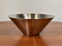 Front view of polished stainless steel conical bowl on wooden surface highlighting the flared lip and smooth surface.