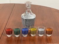 Full set displaying one decanter and six shot glasses with colorful bands, all standing on a wooden surface.