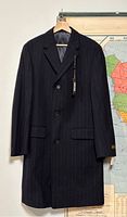 Front view of men's navy blue pinstripe wool overcoat with tags hanging on hanger against wall.