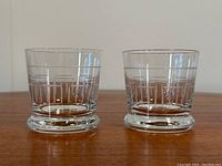 Front view of two crystal old fashioned glasses showing cut geometric line pattern and thick bases on wood surface.