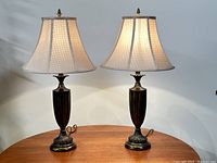 Pair of vintage-style table lamps on a wooden surface against a light wall, with shades illuminated, showing full height and design details.