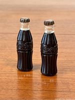 Pair of vintage Coca-Cola mini lighter bottles standing upright on wood surface showing their shape and branding.