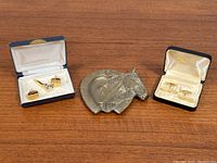 Overview of two sets of vintage brass cufflinks, one set with matching tie clip, and a solid brass horseshoe ashtray featuring a horse head.