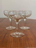Set of three clear cut glass stemware with floral etching on bowl and thin stem with round base on wood surface