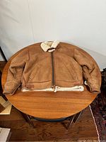 Front view of tan suede leather bomber jacket laid flat