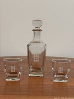Full view of whisky decanter flanked by two whisky glasses on wooden surface, showing etched geometric design on all three pieces.