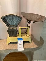 Full view of antique cast iron candy scale showing yellow base, dial face, and weighing pan.