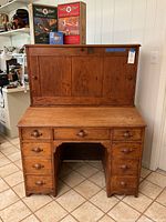 Front photo showing the overall antique wooden postal secretary with hutch, nine drawers, folding desktop, and upper cabinet doors.