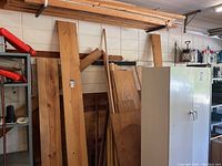 Wide view showing assorted wood pieces leaning against a wall in a garage, including large planks and plywood sheets.